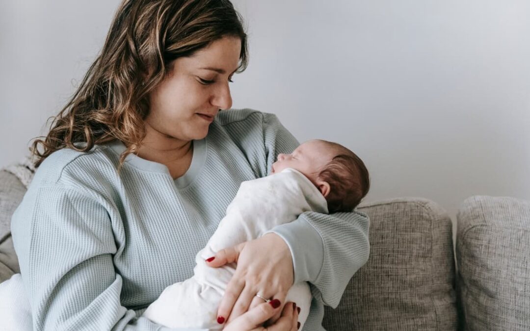 Madre primeriza sosteniendo a su recién nacido en casa, mirándolo con ternura mientras lo envuelve en una manta.