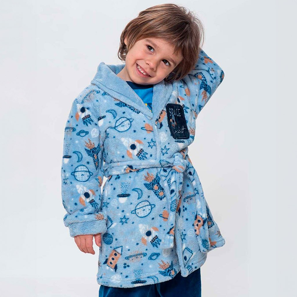 Un niño pequeño con una bata de casa de colores suaves, comprada en elesanbebe.com, sonríe alegremente mientras juega en el suelo. La bata es cómoda y crea una sensación cálida y acogedora en un ambiente hogareño.