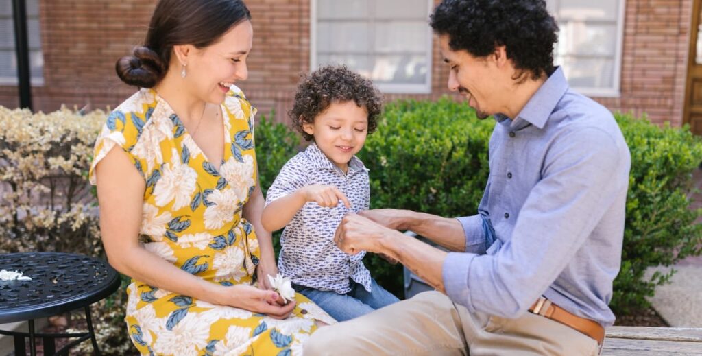 Una familia feliz compuesta por dos padres sonriendo mientras juegan y abrazan a su hijo de dos años en un parque.