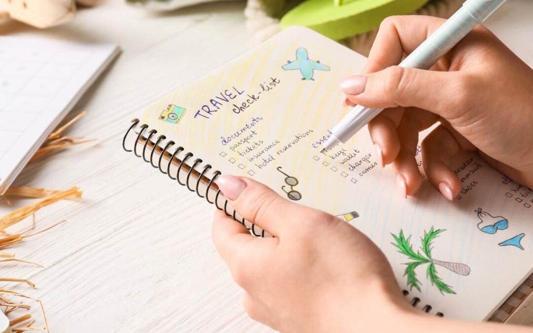 Mujer sentada con su bebé revisando una lista de viaje en una libreta.